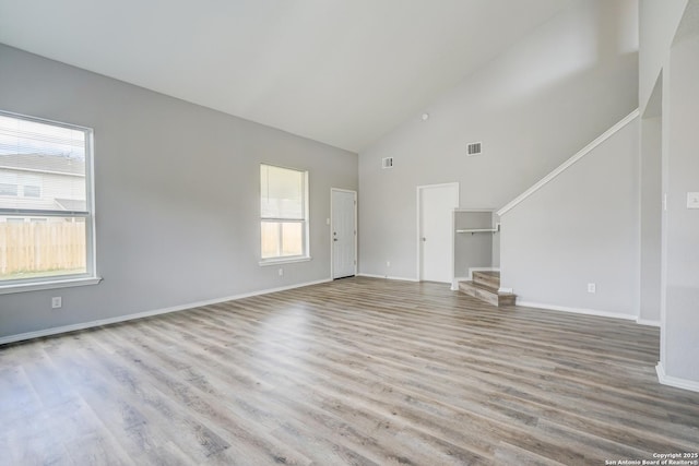 unfurnished living room with visible vents, baseboards, wood finished floors, stairs, and high vaulted ceiling