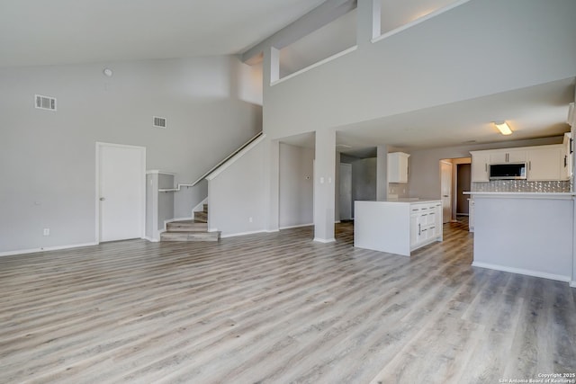 unfurnished living room with stairway, light wood-type flooring, visible vents, and baseboards