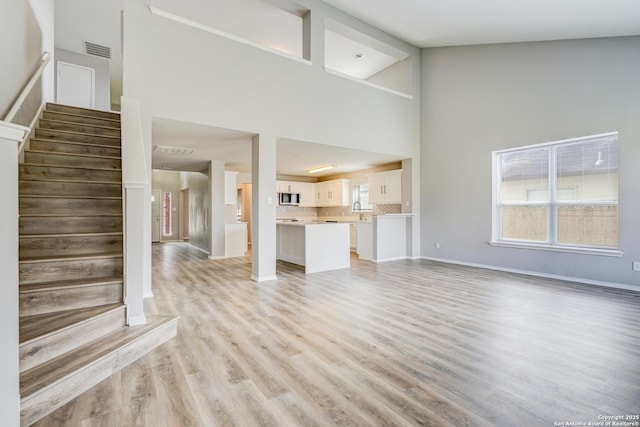 unfurnished living room featuring baseboards, visible vents, stairway, and light wood finished floors