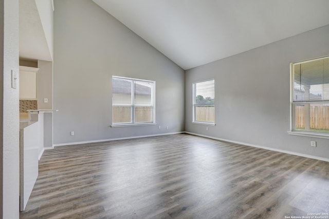 empty room featuring high vaulted ceiling, baseboards, and wood finished floors