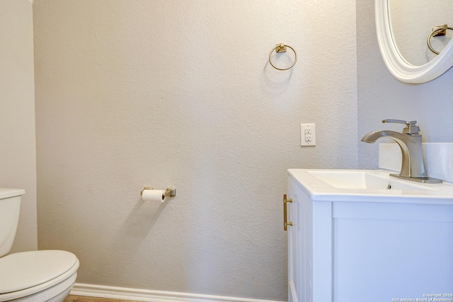 bathroom featuring a textured wall, vanity, toilet, and baseboards