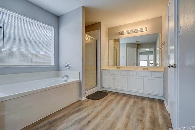 bathroom with double vanity, a shower stall, a bath, and wood finished floors