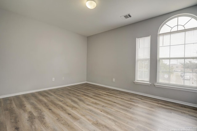 empty room with wood finished floors, visible vents, and baseboards