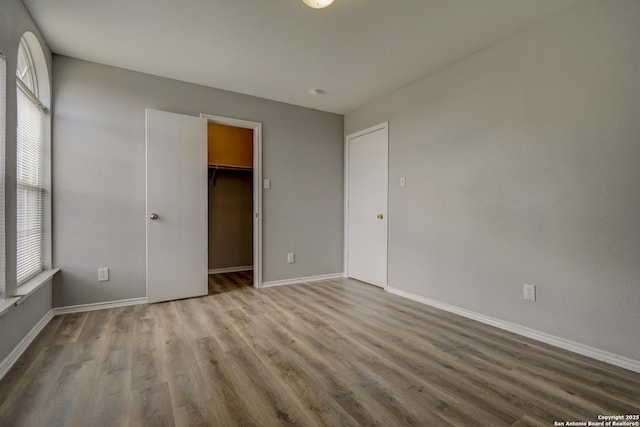 unfurnished bedroom with a closet, a spacious closet, baseboards, and wood finished floors