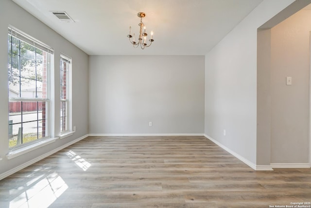 spare room featuring baseboards, light wood-style flooring, visible vents, and an inviting chandelier