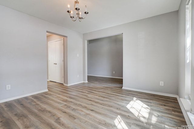 spare room with baseboards, wood finished floors, and a notable chandelier