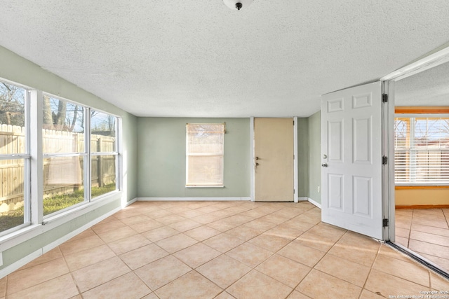 spare room featuring light tile patterned floors, plenty of natural light, and baseboards