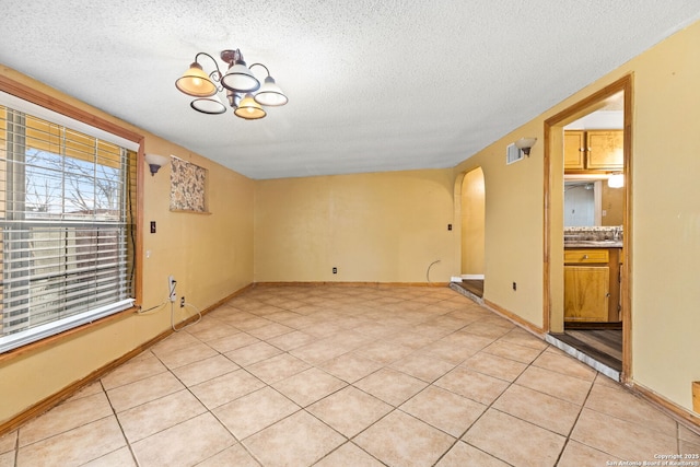 spare room featuring arched walkways, a notable chandelier, light tile patterned floors, a textured ceiling, and baseboards