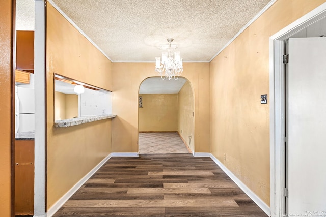 hall with a textured ceiling, arched walkways, crown molding, wood finished floors, and an inviting chandelier