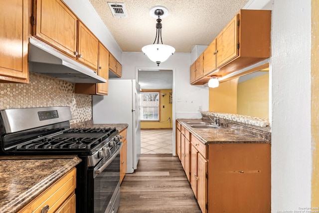 kitchen with decorative backsplash, a textured ceiling, under cabinet range hood, stainless steel range with gas cooktop, and a sink