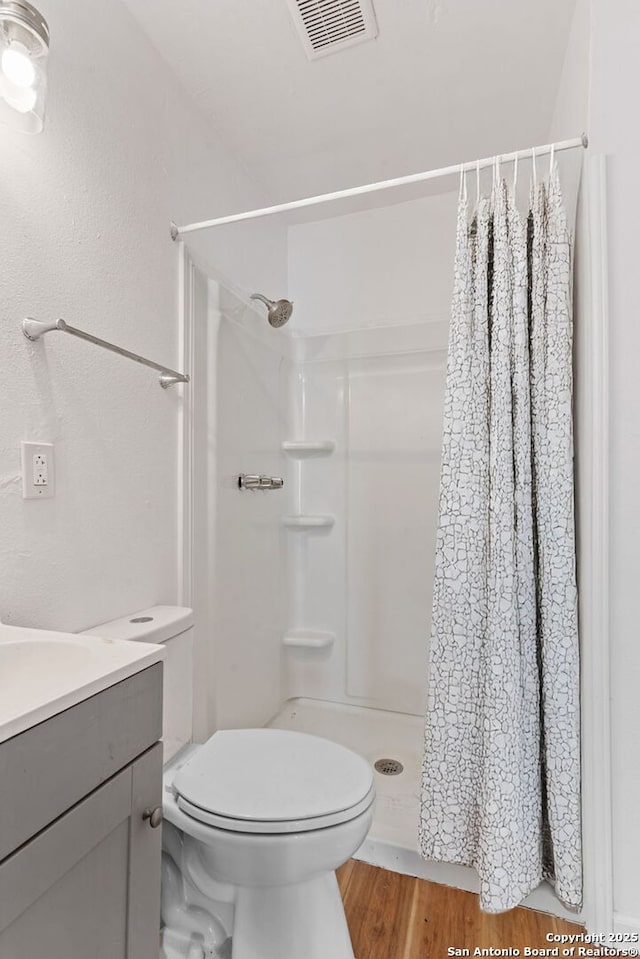bathroom with visible vents, toilet, wood finished floors, vanity, and a shower stall