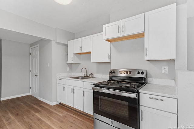 kitchen featuring a sink, baseboards, white cabinets, stainless steel electric stove, and light wood finished floors