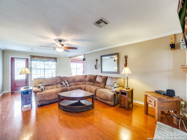 living room with baseboards, visible vents, a ceiling fan, crown molding, and light wood-type flooring