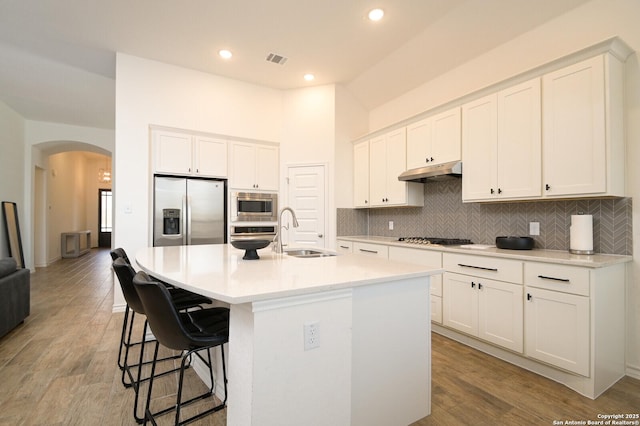 kitchen with arched walkways, under cabinet range hood, stainless steel appliances, a sink, and visible vents