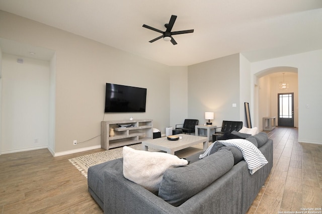 living area with a ceiling fan, baseboards, arched walkways, and wood finished floors