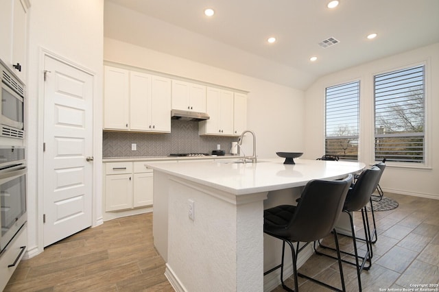 kitchen with a sink, visible vents, white cabinets, decorative backsplash, and a kitchen bar