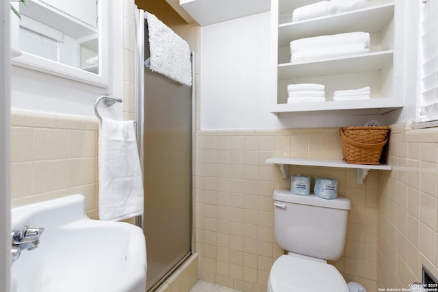 bathroom with toilet, a wainscoted wall, a sink, tile walls, and a stall shower