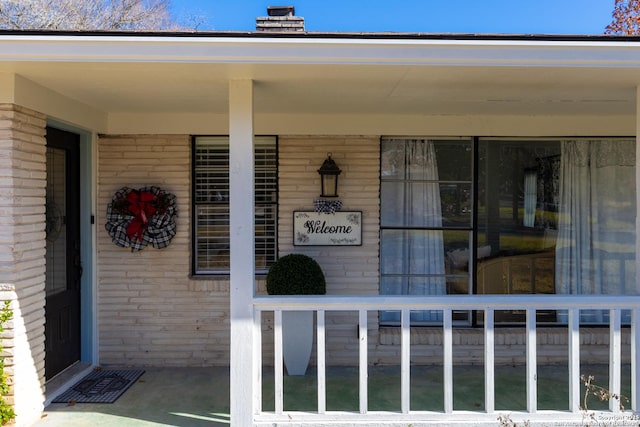 doorway to property featuring a porch, brick siding, and a chimney