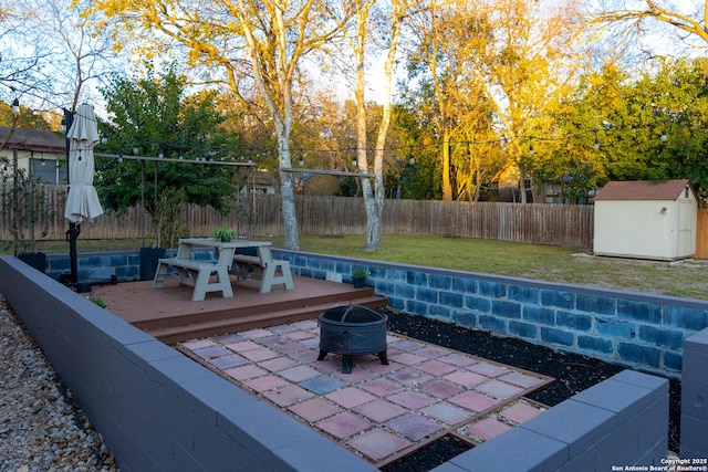 view of patio / terrace with an outbuilding, a storage shed, a deck, a fenced backyard, and a fire pit