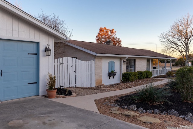 entrance to property featuring a garage, driveway, a chimney, covered porch, and brick siding