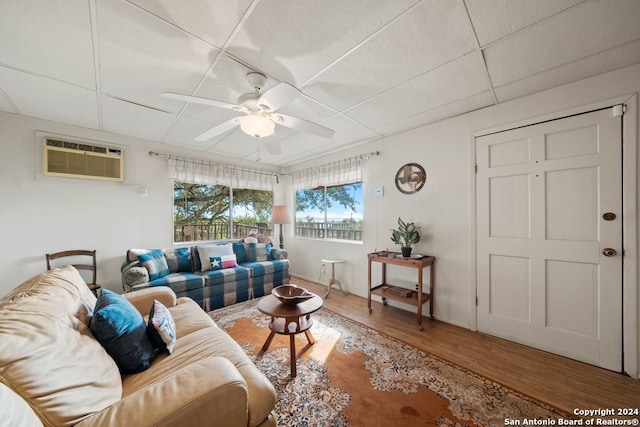 living area featuring a paneled ceiling, a wall unit AC, ceiling fan, and wood finished floors