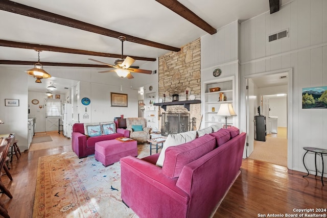 living room with beam ceiling, wood-type flooring, visible vents, ceiling fan, and a stone fireplace