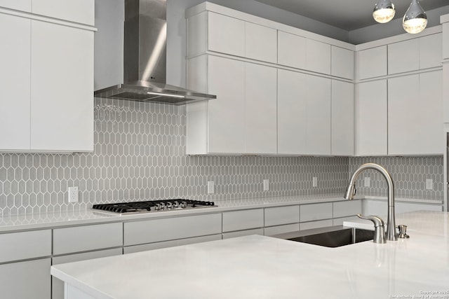 kitchen featuring backsplash, light countertops, a sink, and wall chimney range hood