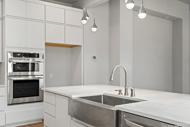 kitchen featuring decorative light fixtures, stainless steel appliances, light countertops, white cabinetry, and a sink