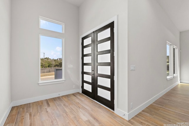 foyer entrance with french doors, light wood-type flooring, a towering ceiling, and baseboards