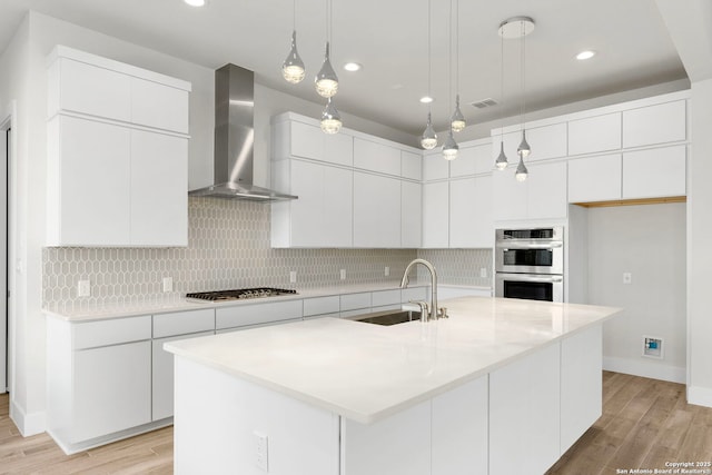 kitchen featuring a sink, wall chimney range hood, double oven, gas cooktop, and backsplash