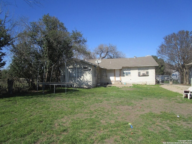 rear view of property with a yard, a trampoline, and fence