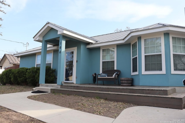 view of front of house with a standing seam roof, a porch, metal roof, and stucco siding