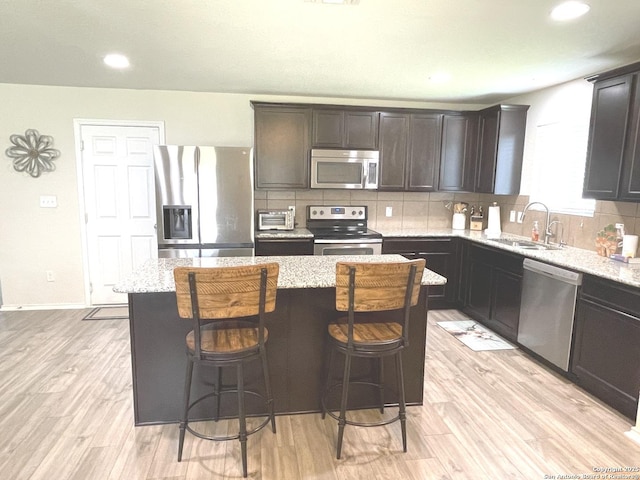 kitchen with a sink, light wood-style floors, appliances with stainless steel finishes, backsplash, and light stone countertops