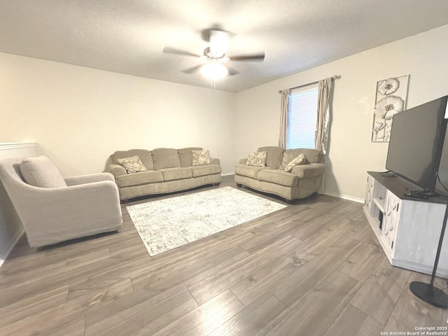 living room featuring ceiling fan, a textured ceiling, baseboards, and wood finished floors