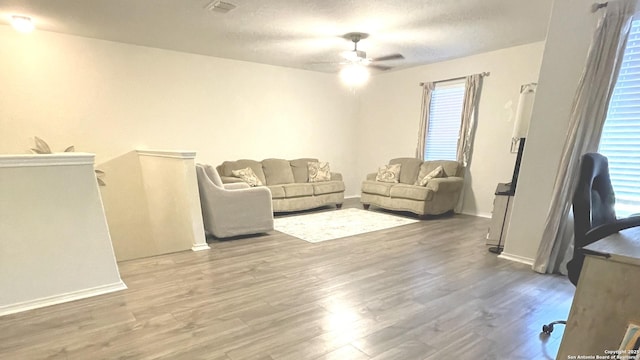 living area with a textured ceiling, wood finished floors, a ceiling fan, and baseboards