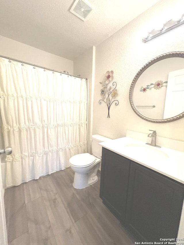 full bath featuring visible vents, toilet, wood finished floors, a textured ceiling, and vanity