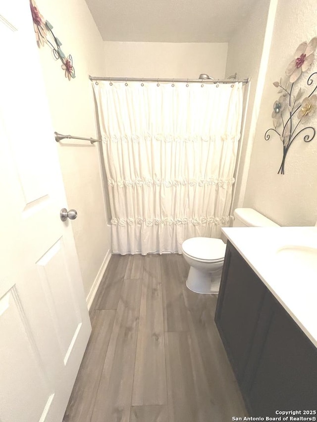 bathroom with toilet, vanity, wood finished floors, a shower with curtain, and baseboards