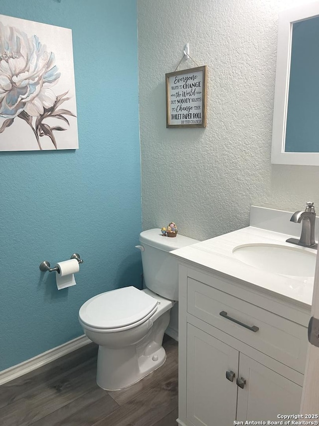 bathroom featuring a textured wall, toilet, vanity, wood finished floors, and baseboards