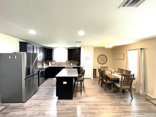 kitchen featuring a breakfast bar area, stainless steel appliances, a kitchen island, a sink, and visible vents