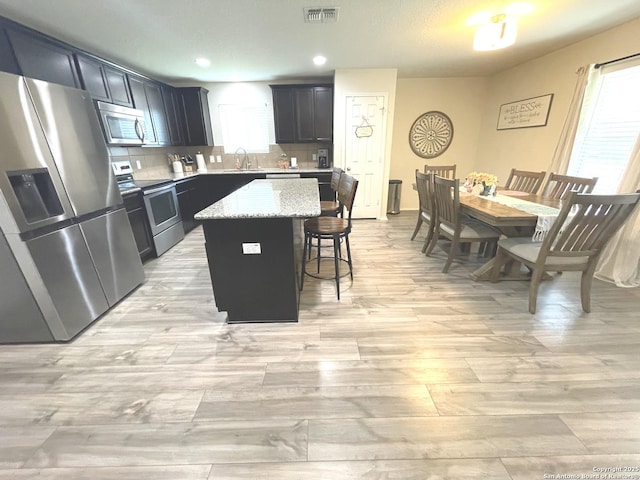 kitchen with visible vents, appliances with stainless steel finishes, a center island, a kitchen bar, and a sink