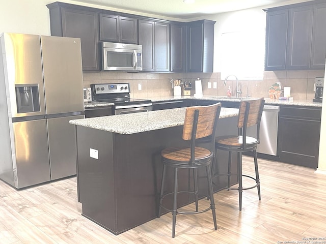 kitchen featuring stainless steel appliances, tasteful backsplash, light wood-type flooring, and a sink