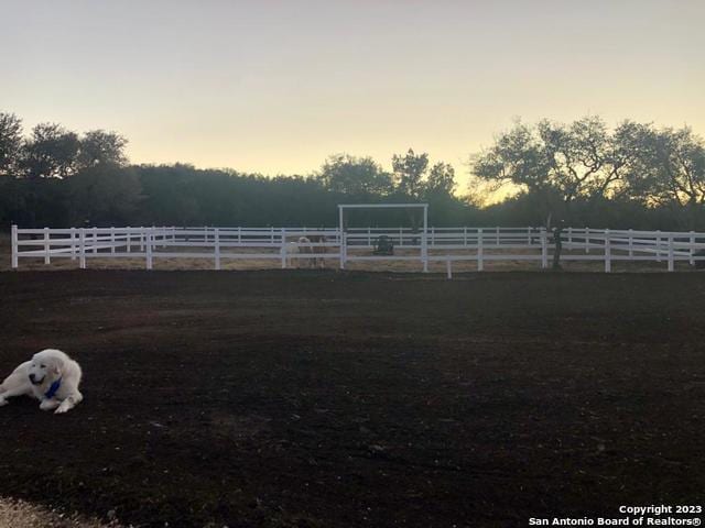 yard at dusk featuring a rural view and fence