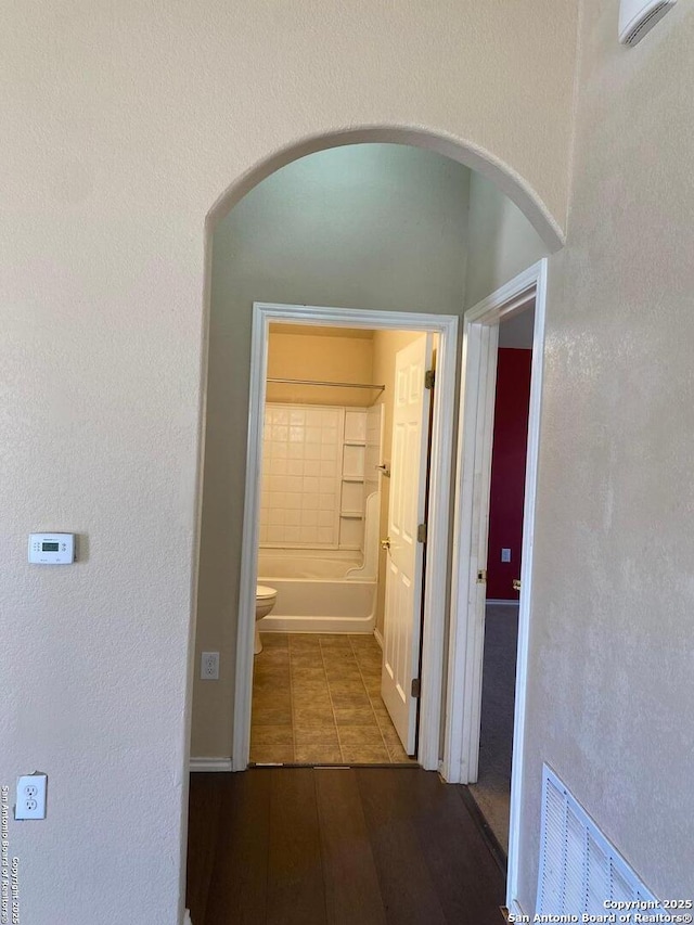 hallway with visible vents, arched walkways, wood finished floors, and a textured wall