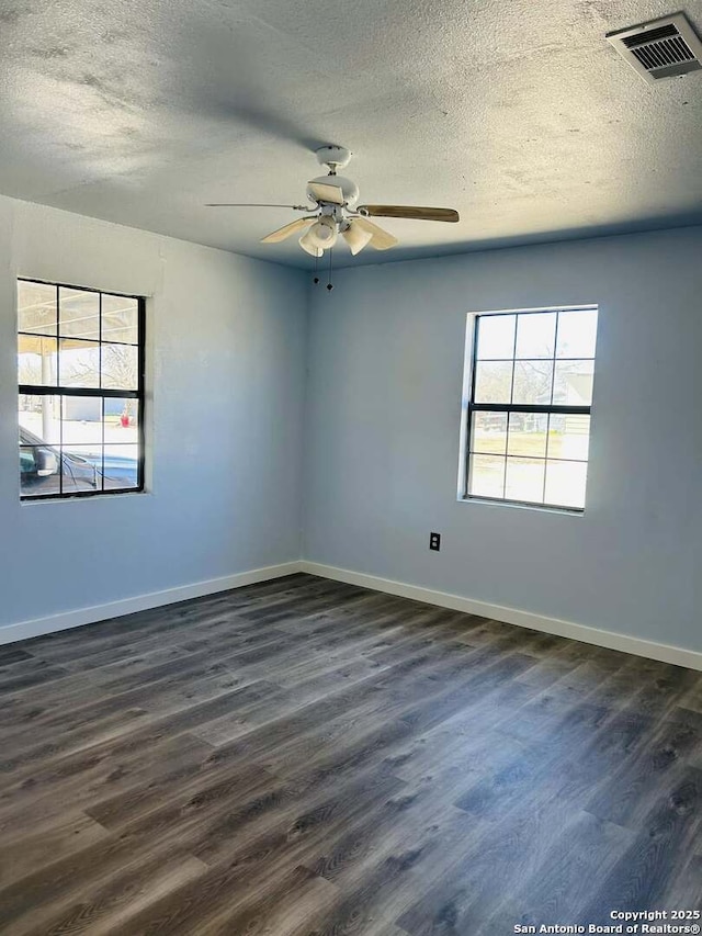 spare room featuring a textured ceiling, a ceiling fan, visible vents, baseboards, and dark wood-style floors