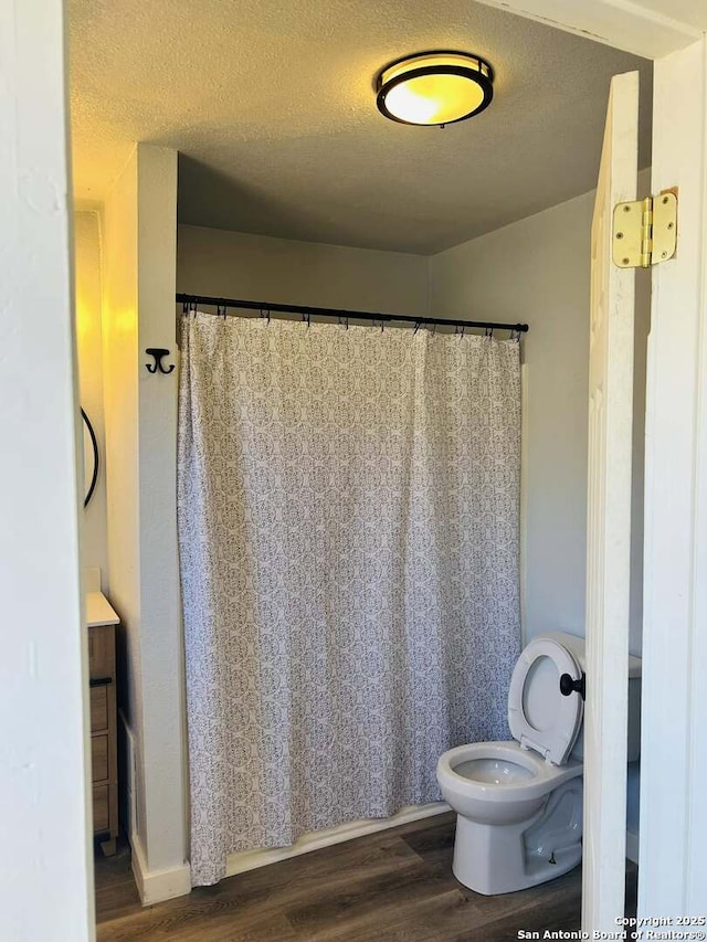 full bath featuring a shower with curtain, a textured ceiling, toilet, and wood finished floors