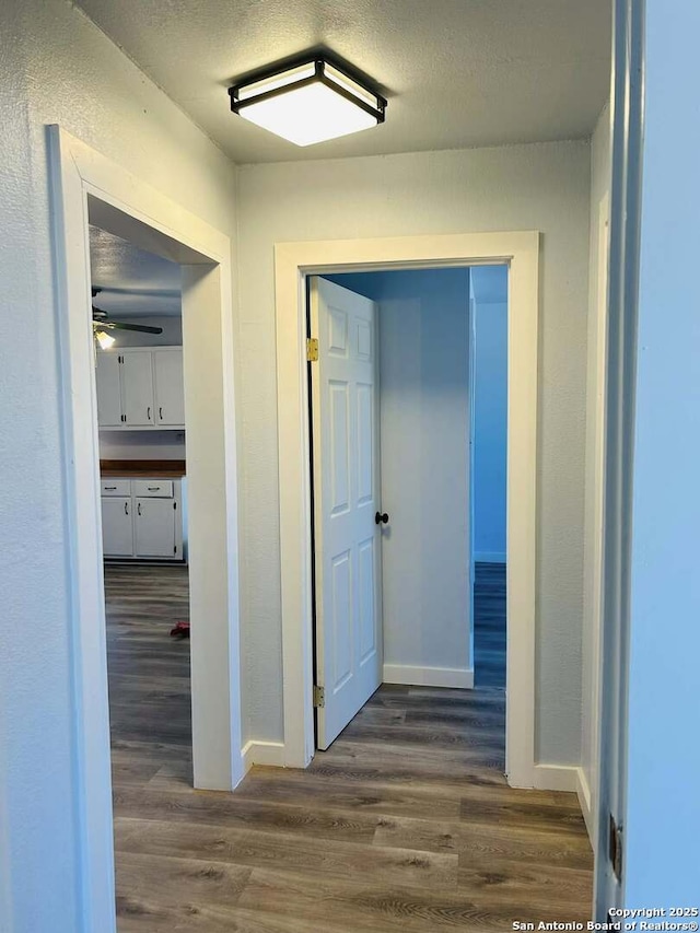 hall featuring a textured ceiling, wood finished floors, and baseboards