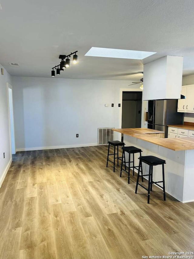 kitchen featuring a breakfast bar, a skylight, visible vents, wooden counters, and freestanding refrigerator