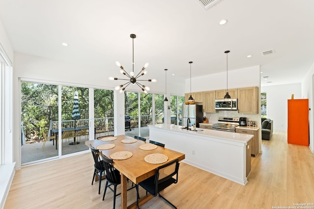 kitchen with a center island with sink, stainless steel appliances, visible vents, light wood-style flooring, and a sink