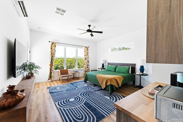 bedroom with light wood-style flooring, visible vents, ceiling fan, and an AC wall unit