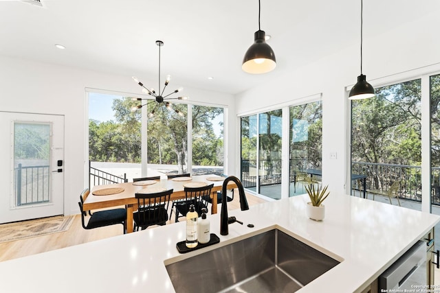 kitchen with wood finished floors, light countertops, a chandelier, pendant lighting, and a sink